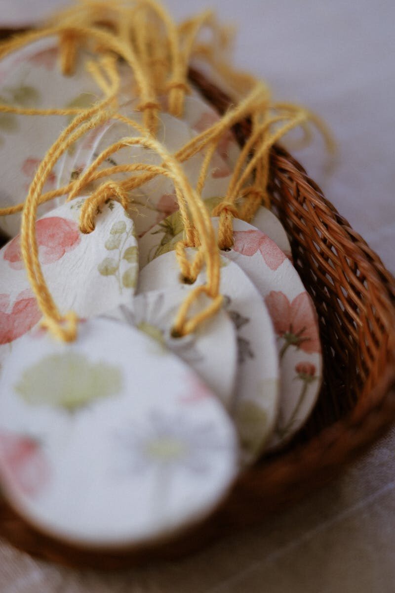 Set of floral ceramic tags with yellow string, placed in a wicker basket, on a table.
